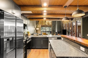A modern kitchen with stainless steel appliances, wooden ceiling beams, and pendant lighting.