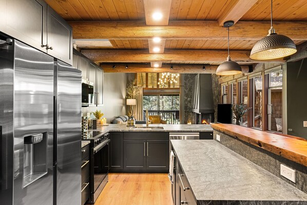 A modern kitchen with stainless steel appliances, wooden ceiling beams, and pendant lighting.