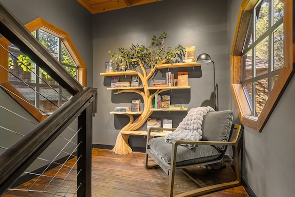 A cozy reading nook with a unique tree-shaped bookshelf, a comfortable chair, and a view through a window.