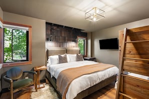 A bedroom with a bed, a TV, a chair, and a wooden ladder.