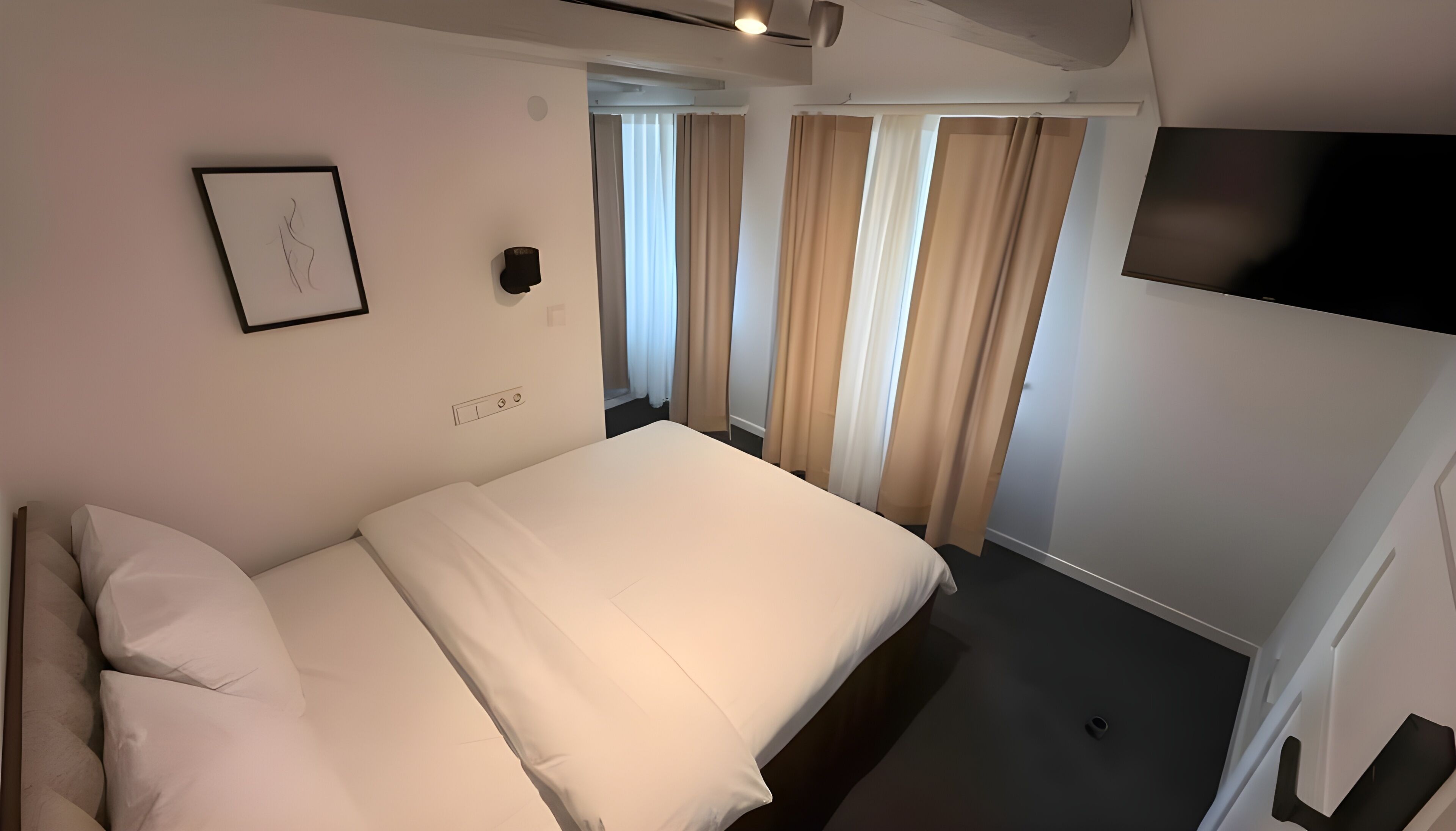 A hotel room with a bed, a TV mounted on the wall, and a door leading to another room.