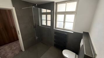 A modern bathroom with a glass-enclosed shower, a toilet, and a window.