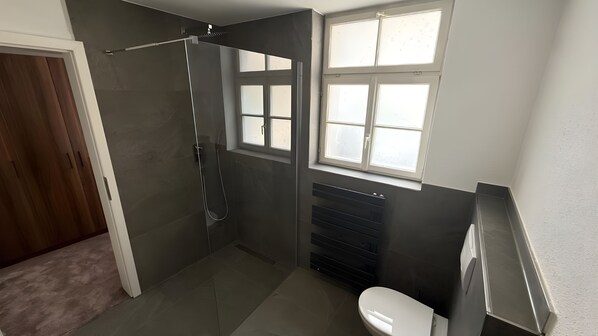 Un baño moderno con cabina de ducha de vidrio, inodoro y ventana.