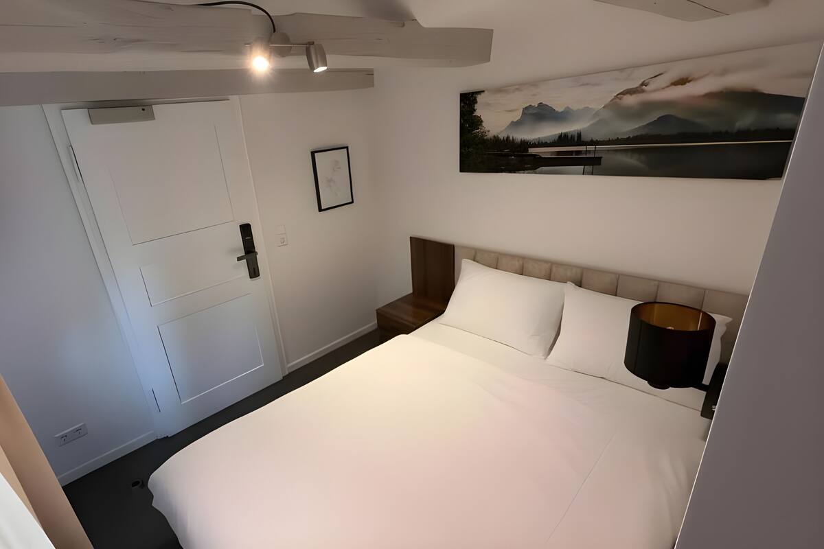Un dormitorio con cama, mesita de noche, lámpara, cuadro y armario.