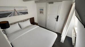 Una habitación de hotel con cama, mesita de noche, lámpara, puerta y un cuadro colgado en la pared.