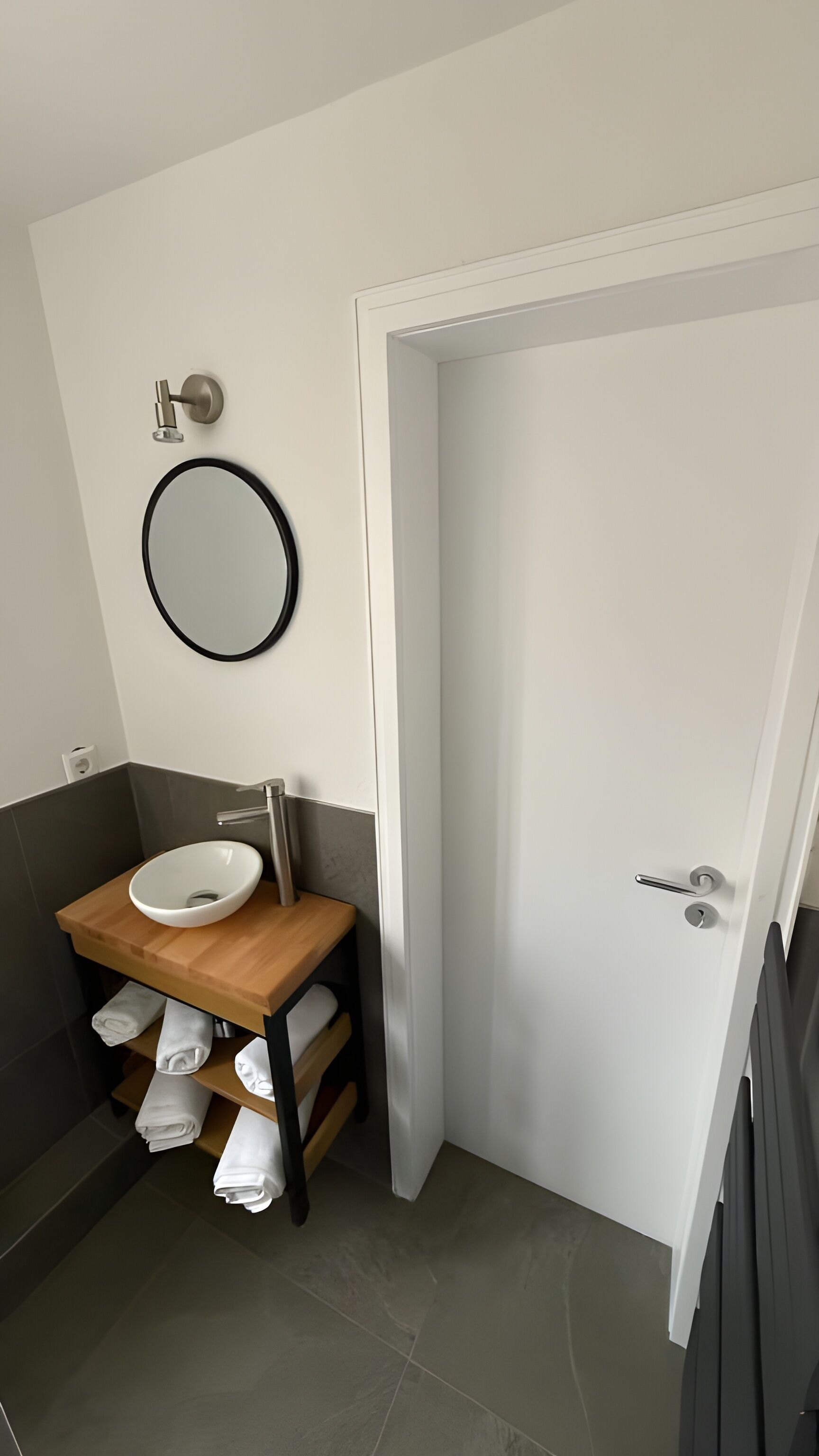 A bathroom with a white sink, a round mirror, and a door.