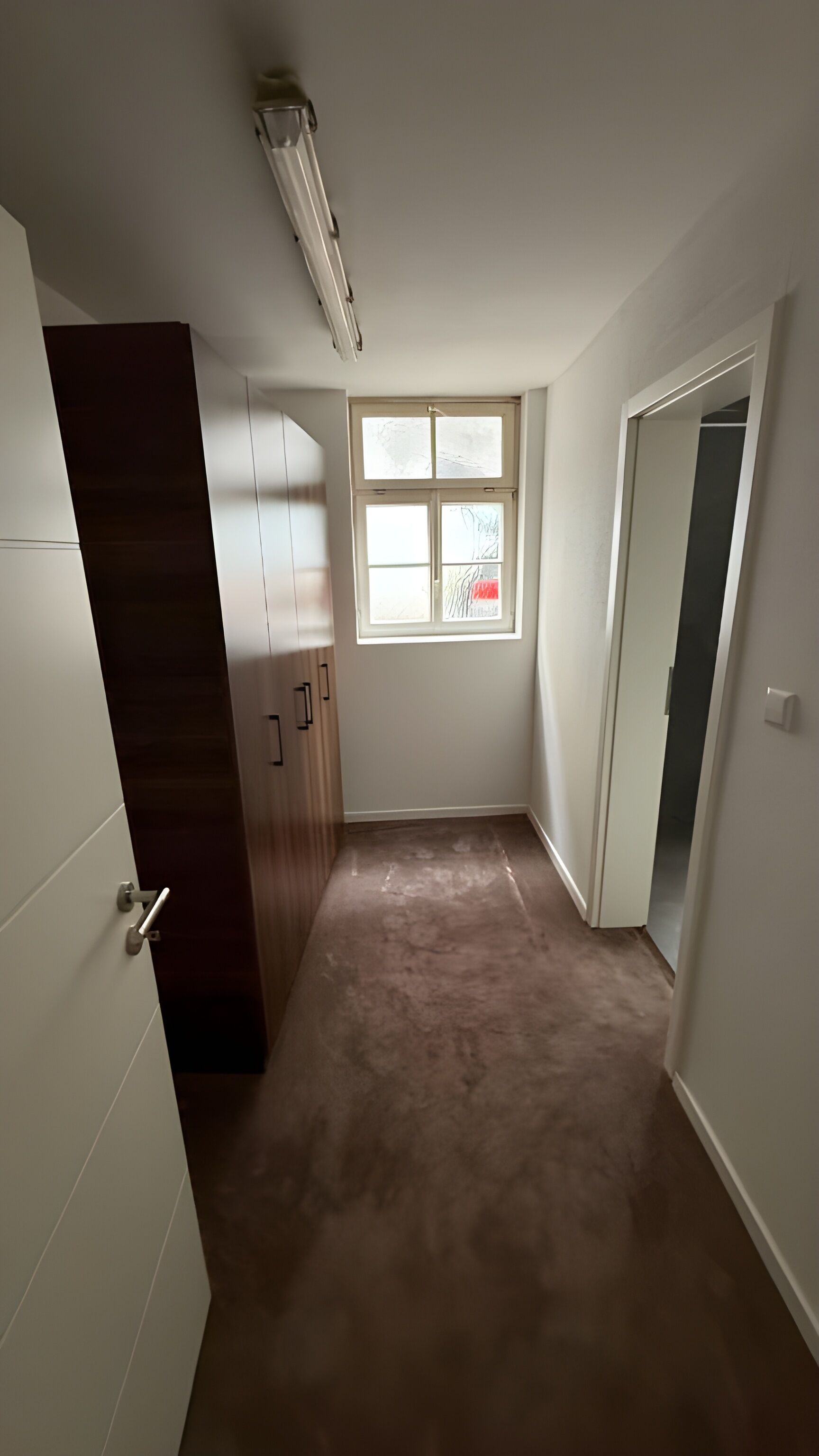Een kamer met een raam, een deur en een vloerbedekking.