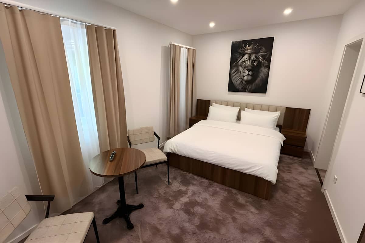 Habitación de hotel con cama, una mesita, una silla y un cuadro en la pared.