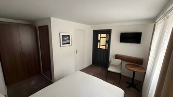 Une chambre à coucher comprenant un lit, une armoire, un bureau avec une chaise, une télévision et une porte avec une fenêtre.