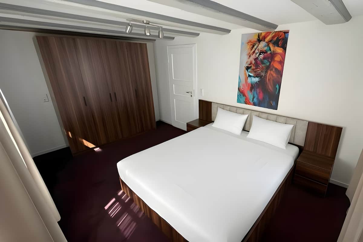 Una habitación de hotel con una cama, cabecera de madera, un cuadro en la pared y una ventana con cortinas.