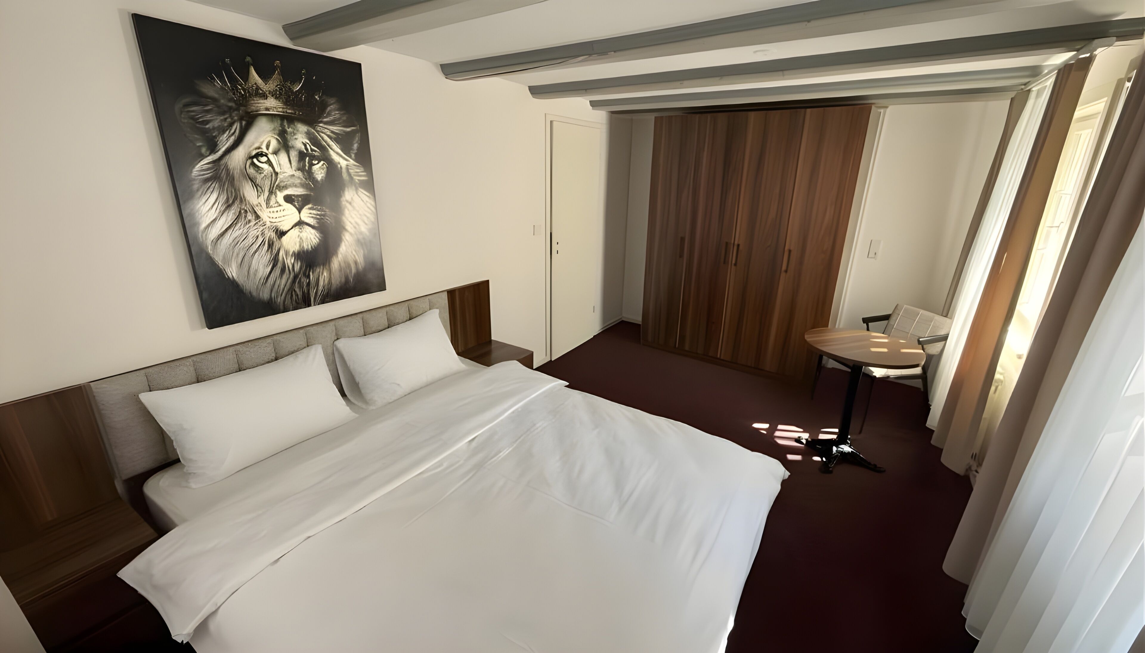 Habitación de hotel con una cama grande, una mesita pequeña, un espejo y una puerta que da a un armario de madera.