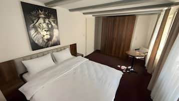 Habitación de hotel con una cama grande, una mesita pequeña, un espejo y una puerta que da a un armario de madera.