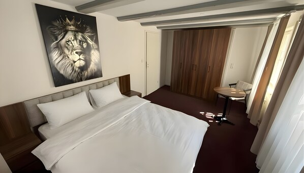 Habitación de hotel con una cama grande, una mesita pequeña, un espejo y una puerta que da a un armario de madera.