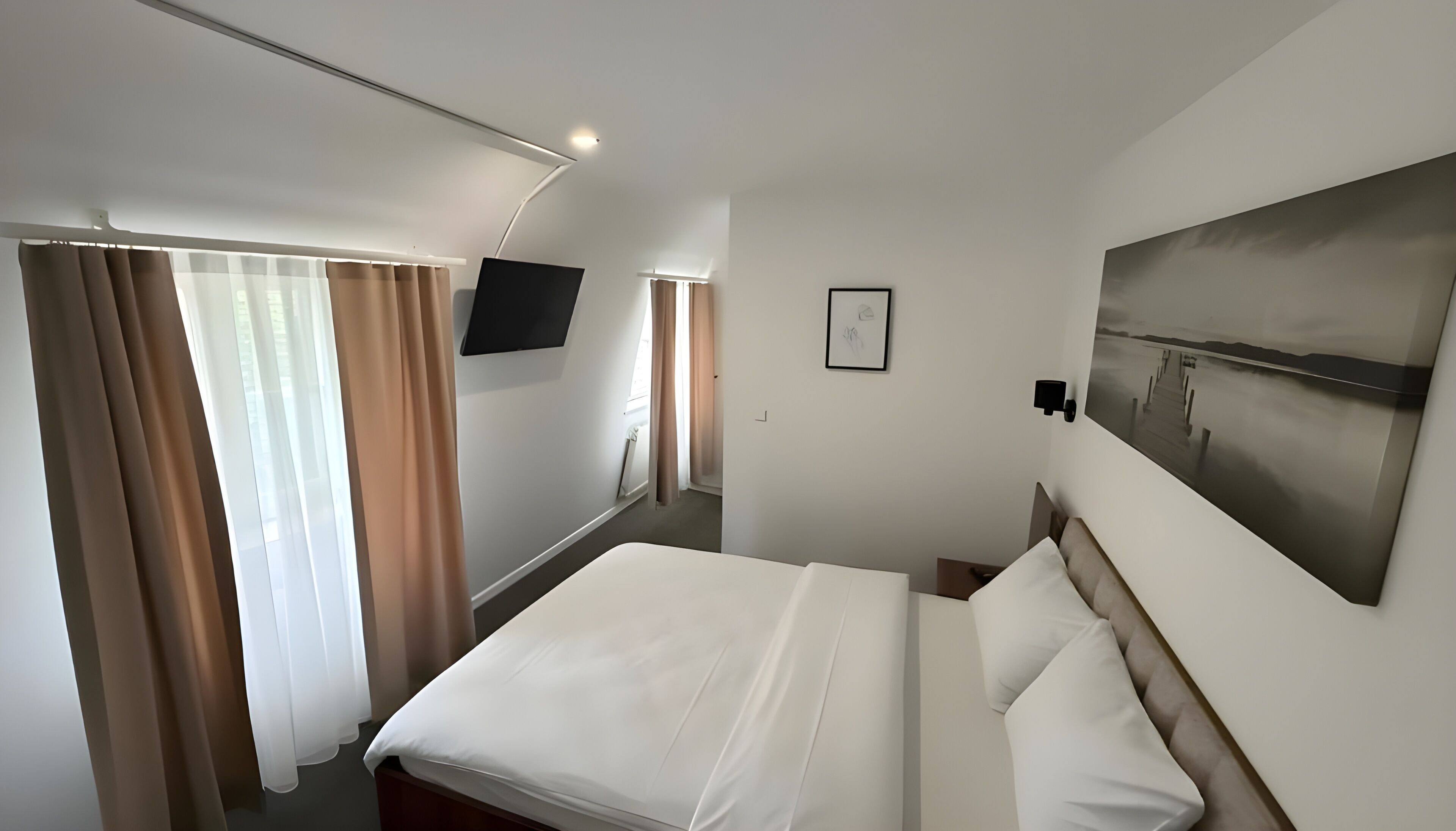 A hotel room with a bed, curtains, a TV, a painting, and a window.