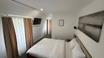 A hotel room with a bed, curtains, a TV, a painting, and a window.