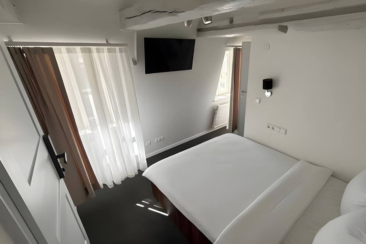 Un dormitorio moderno con cama, televisor de pantalla plana, ventana con cortinas y radiador.