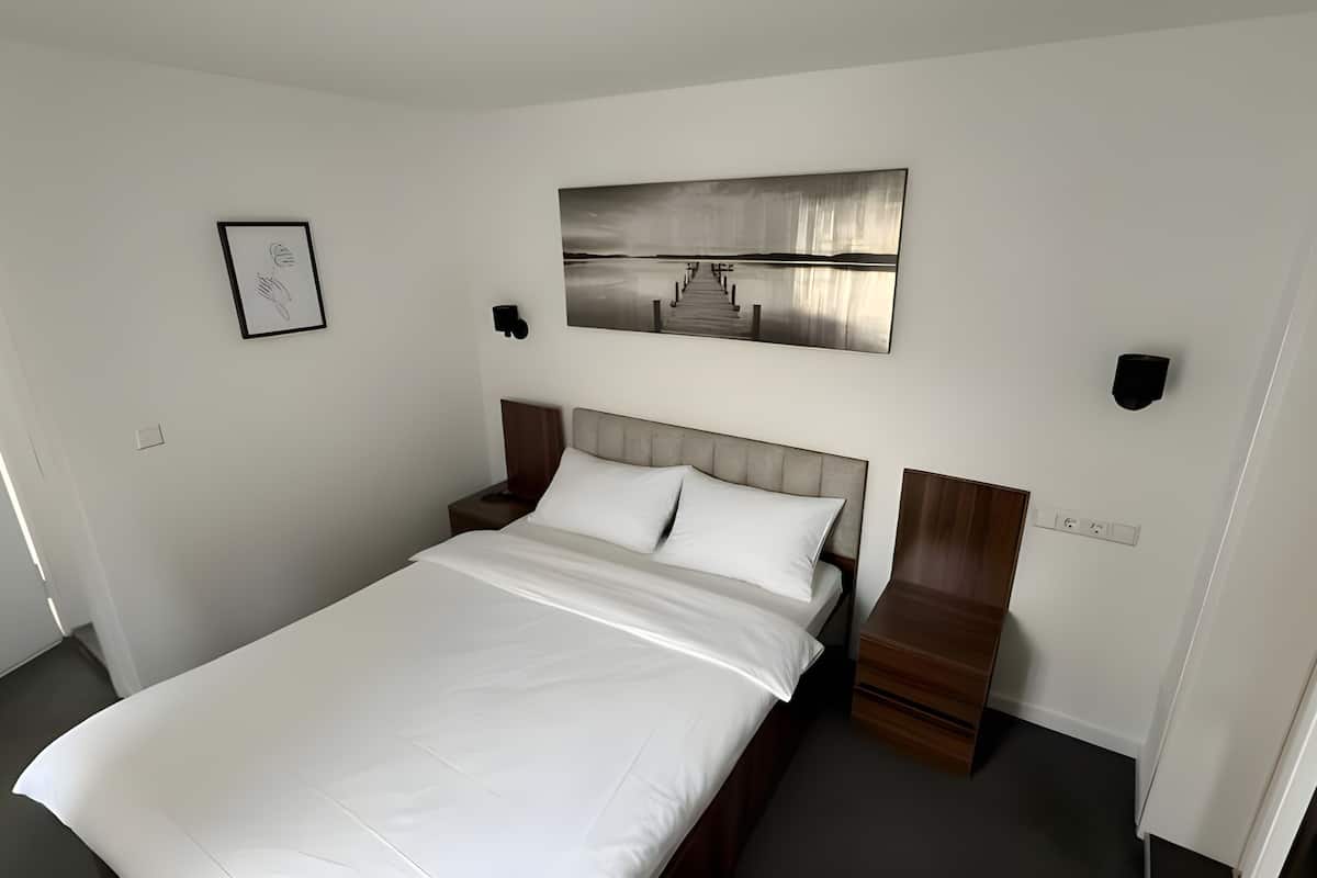Una habitación de hotel con cama, mesita de noche, lámpara de pared y un cuadro.