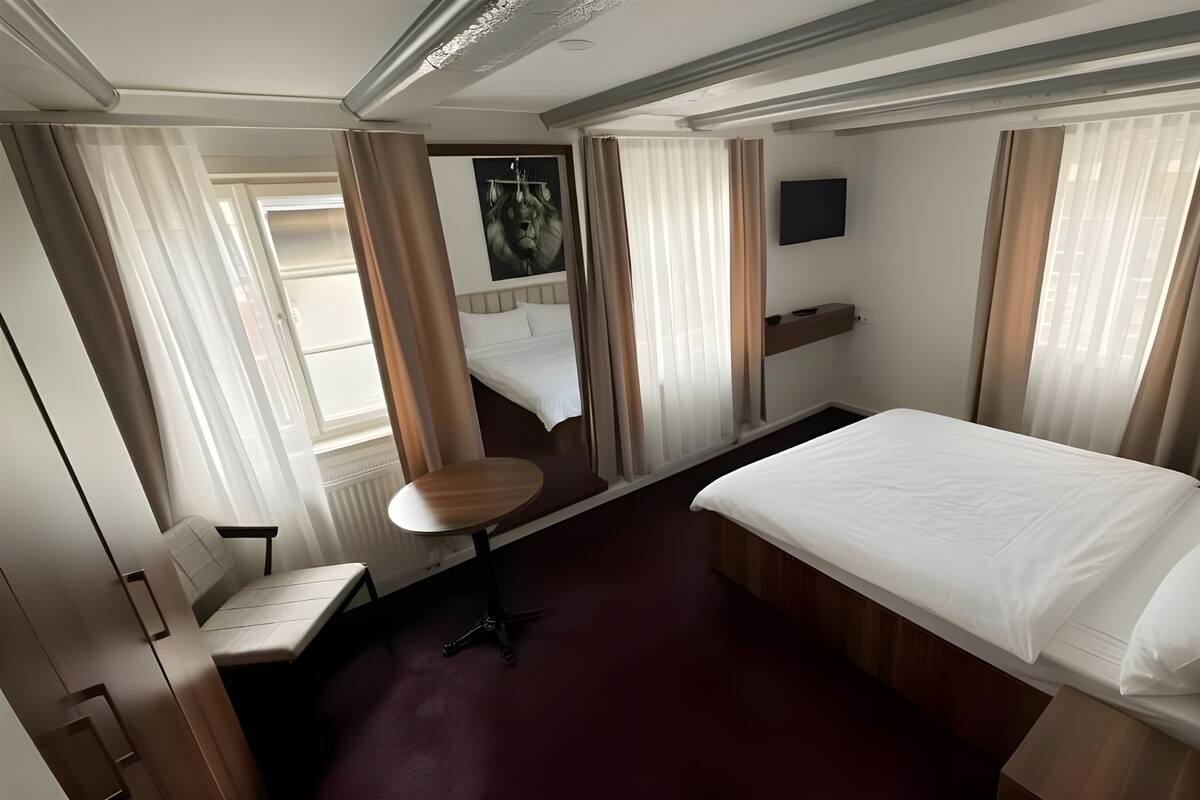 Habitación de hotel con cama, escritorio, silla, televisor y ventana con cortinas.