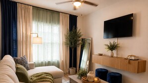 Una sala de estar con un sofá, una mesa de centro, un televisor, un ventilador de techo y una planta.
