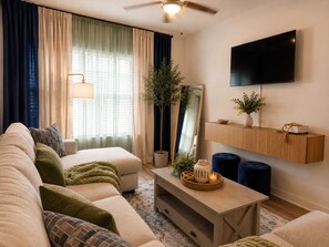 A living room with a sofa, a coffee table, a TV, a ceiling fan, and a plant. - Luxury 2BR Retreat Near FIFA World Cup & Mercedes-Benz Stadium (Atlanta)