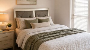 Un dormitorio con cama, mesita de noche, lámpara y un cuadro en la pared.