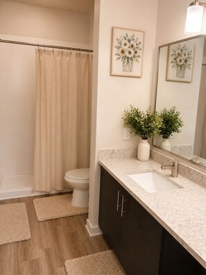 Un bagno con tenda della doccia, water, lavandino, specchio e piante decorative.