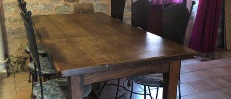 Een rustieke stenen muur, een houten eettafel met metalen stoelen, en een raam met gordijnen.