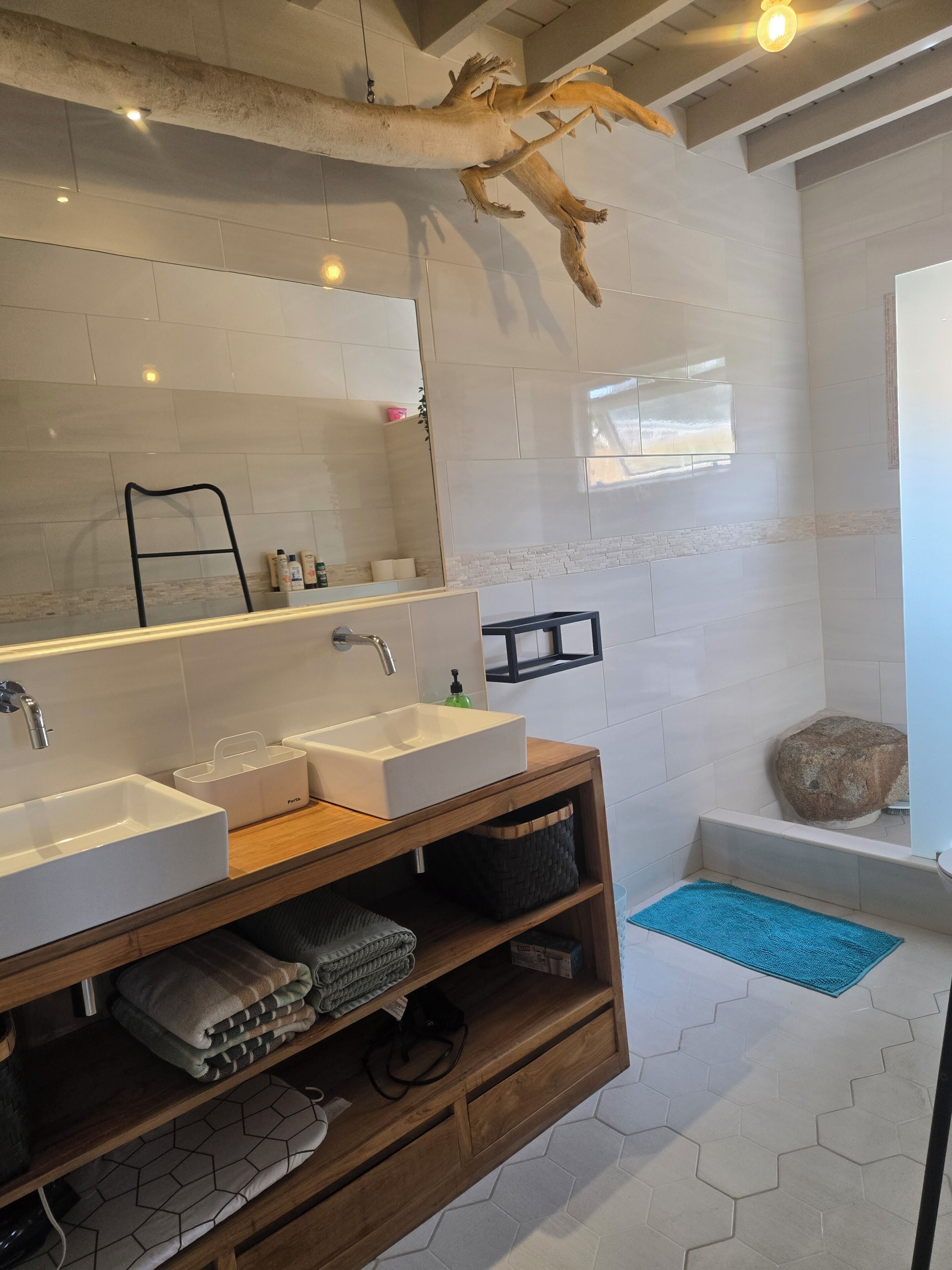 Un baño moderno con un espejo grande, dos lavamanos, un mueble de tocador de madera y una zona de ducha.