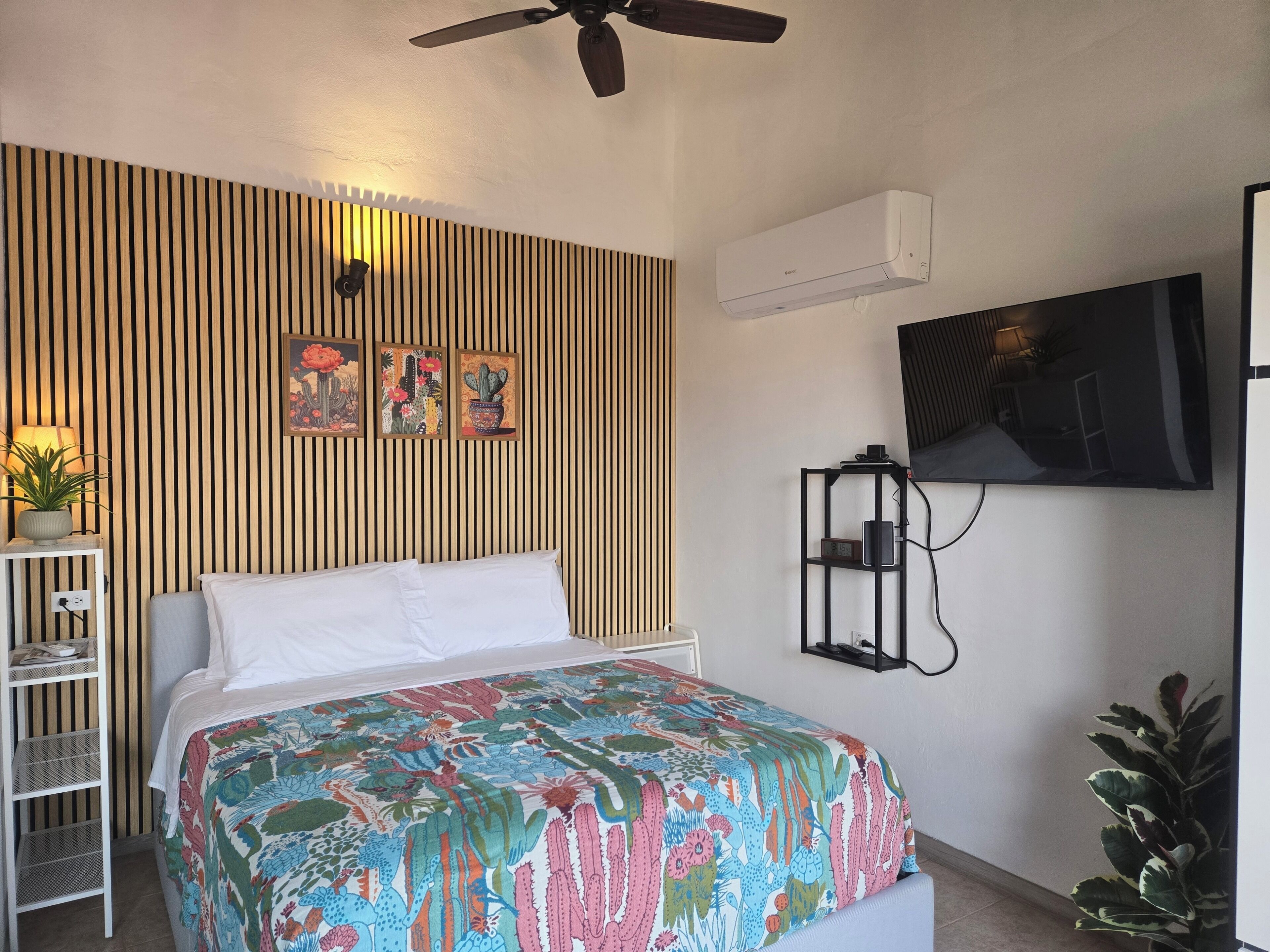 Un dormitorio con cama, televisor montado en la pared, ventilador de techo y aire acondicionado mural.