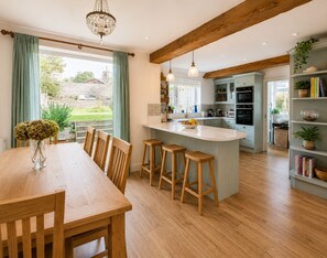 Una cocina moderna con vigas de madera, una isla central, taburetes de bar y una zona de comedor con mesa y sillas.