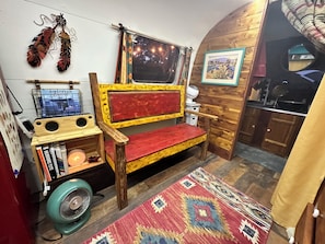Une pièce chaleureuse avec un banc en bois, un petit ventilateur, une bibliothèque et un tapis à motifs.
