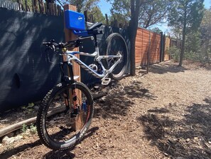 Un vélo tout-terrain est garé contre une clôture en bois, dans une zone boisée.