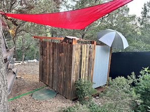 Une petite construction en bois, dotée d’une extension en métal ondulé, d’un auvent rouge et d’un tuyau d’arrosage vert.
