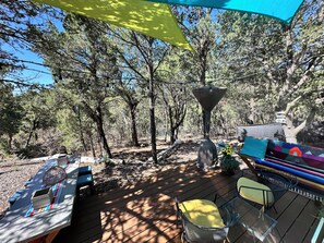Um deck com mobiliário de exterior, um lustre pendurado e vista para uma área arborizada.