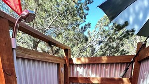 Une terrasse en bois avec une rambarde en métal, un petit conteneur rose et un banc en bois.