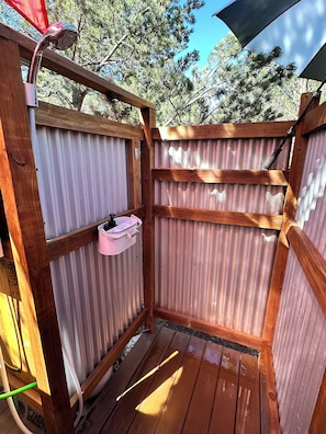 Una terraza de madera con barandilla de metal, un pequeño recipiente rosa y un banco de madera.