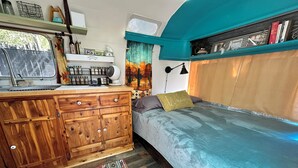 Un intérieur de camping-car compact et bien aménagé, comprenant un coin cuisine, un lit et une fenêtre.