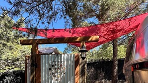 Une petite construction en bois, dotée d’une porte en métal, d’un auvent rouge et d’un véhicule garé à proximité.