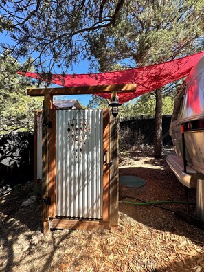 Eine kleine Holzhütte mit einer Metalttür und einem roten Vordach, in der Nähe steht ein Fahrzeug.
