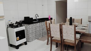 A compact kitchen with a gas stove, sink, and microwave, a dining area with a table and chairs, and a small refrigerator. - Comfort and Style | 7 Min Walk from Parque do Povo. (Campina Grande)