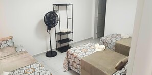 A room with two beds, a standing fan, a shelf unit, and a door. - Comfort and Style | 7 Min Walk from Parque do Povo. (Campina Grande)
