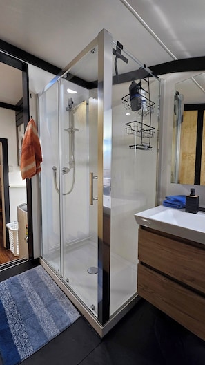 Un bagno moderno con doccia vetrata, lavandino bianco e mobile contenitore in legno.