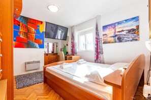 Una habitación de hotel con una cama, televisión, un cuadro, una ventana y un escritorio.