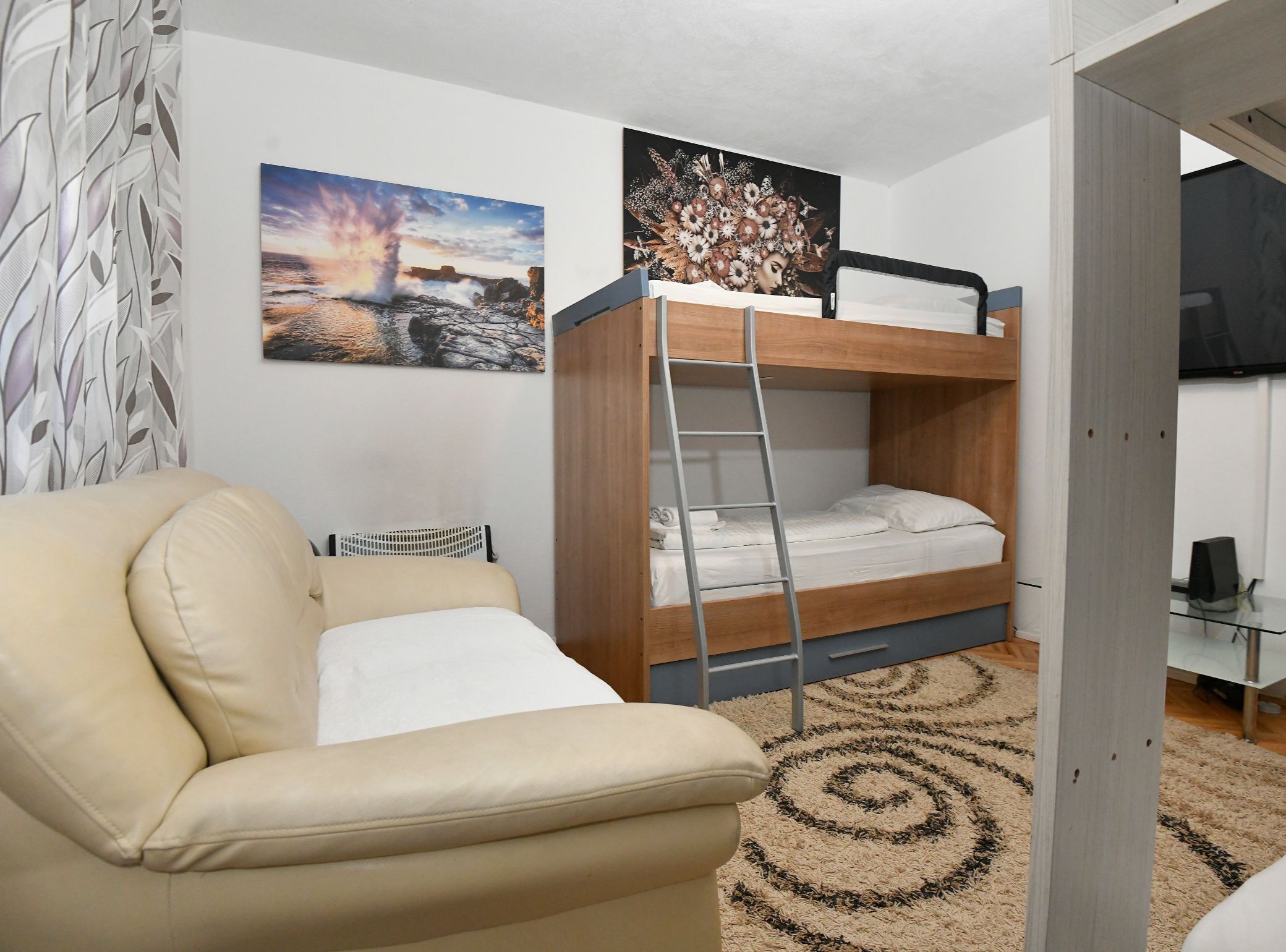 A bunk bed with a ladder, a sofa, a painting of a sunset, and a television.