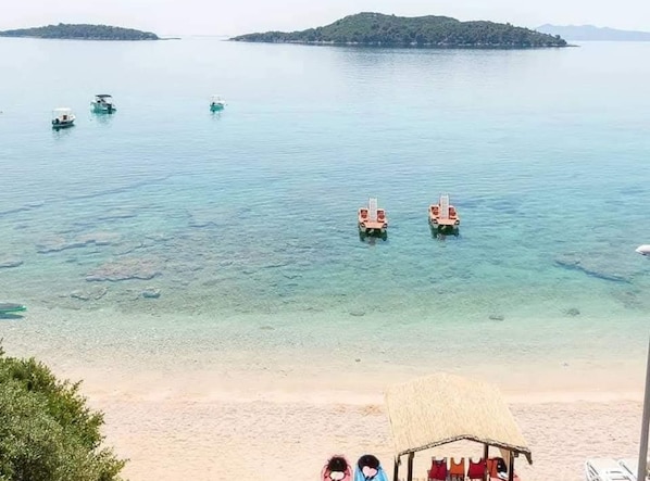 Ein Strand mit klarem Wasser, einer Reetdachhütte und einem kleinen Boot.