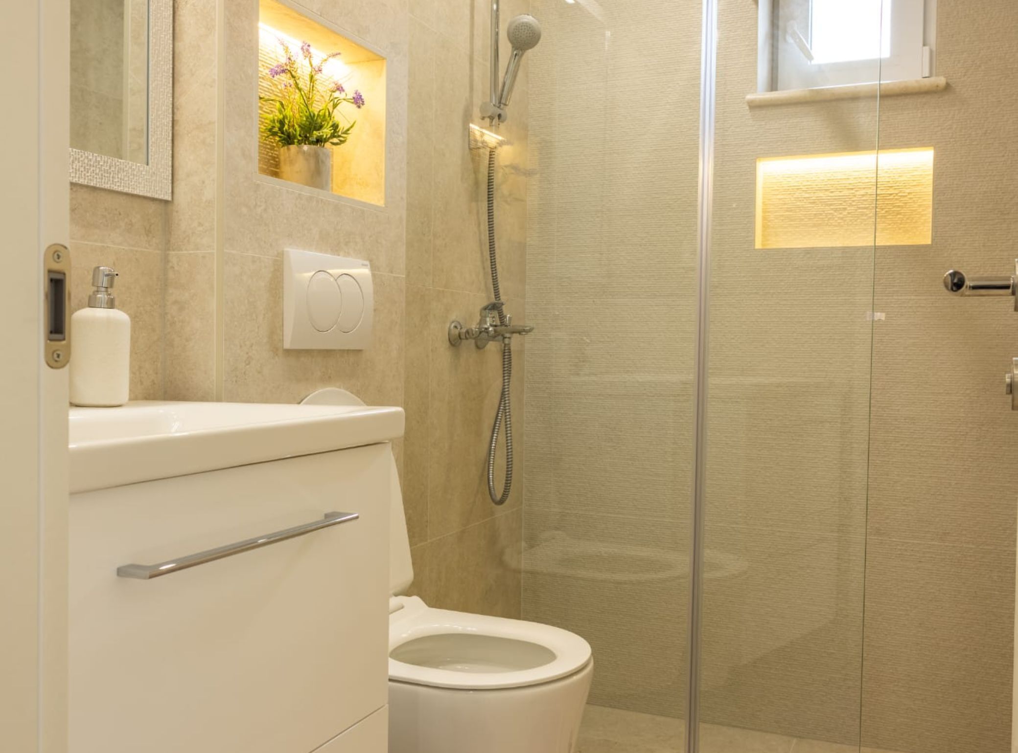 A bathroom with a toilet, a shower, a sink with a mirror, and a potted plant.