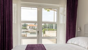A hotel room with a bed, a view of a building across a body of water, and a balcony with a railing. - Apartman Helena Korčula (Blato)
