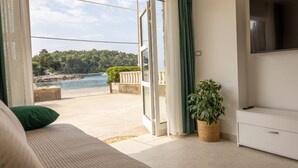 A room with a bed, a TV, a plant, and a view of a body of water and greenery. - Apartman Helena Korčula (Blato)