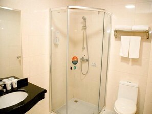 Eine Duschkabine mit Glaswänden, eine Handbrause, ein Waschbecken mit schwarzer Ablagefläche und eine Toilette mit weißem Tank.