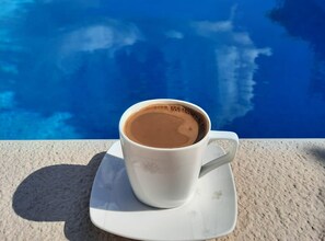 Eine weiße Kaffeetasse auf einem Untertasse neben einem Pool mit klarem, blauem Wasser.
